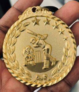 Close-up of a gold cricket medal showcasing intricate design details, held in a hand.